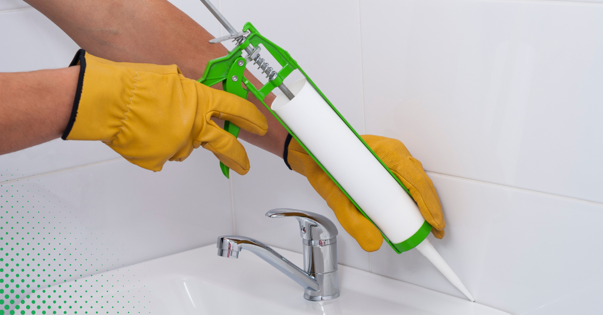 A person wearing gloves applies caulk along a bathroom sink edge for effective waterproofing.