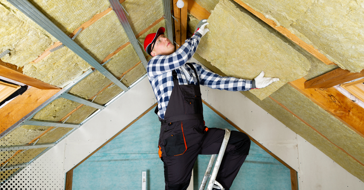 Worker installing insulation panels in an attic ceiling.