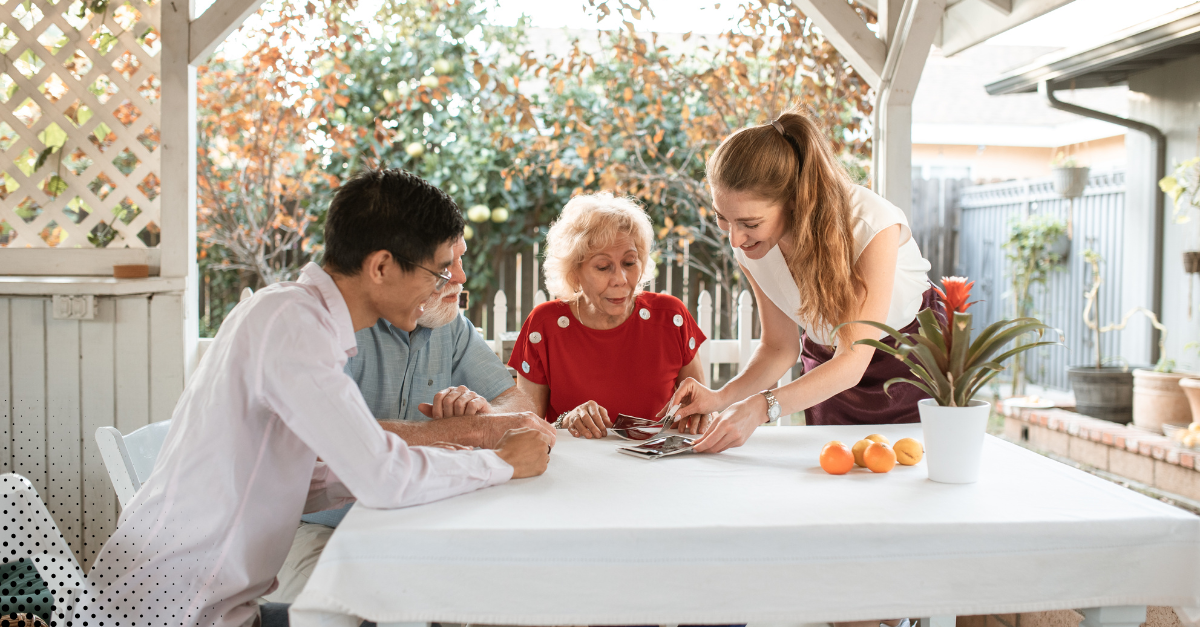 Diverse group of people gathered around a table outdoors looking at photos and smiling.
