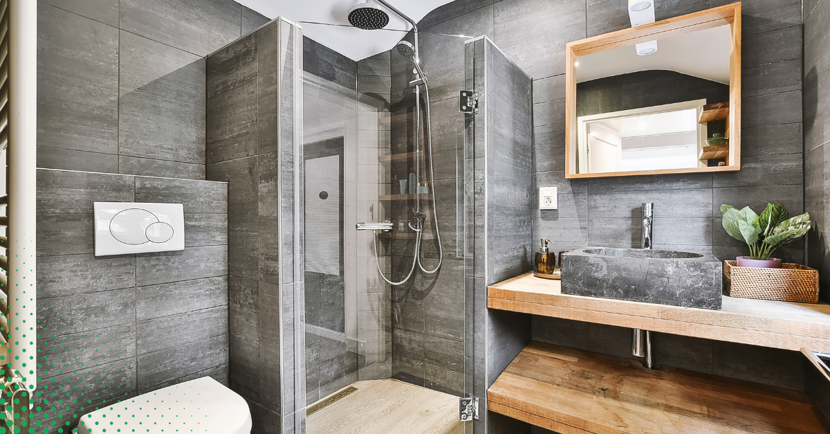 A modern bathroom design with sleek dark tiles, a walk-in glass shower, and a wooden vanity with a stone sink.