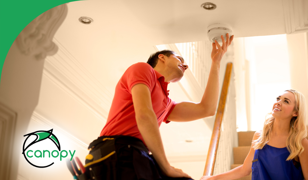 Home maintenance professional inspecting a smoke detector for safety and functionality in a modern home staircase.