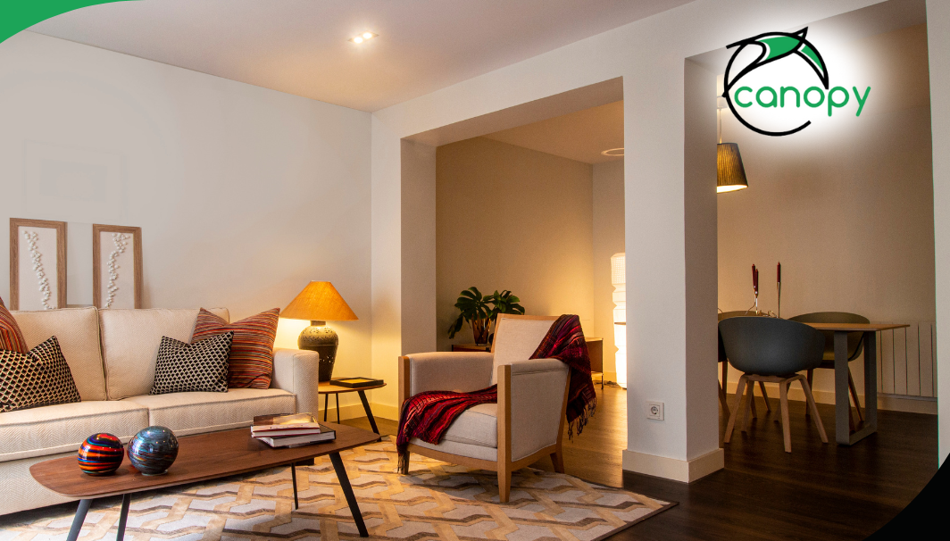 A modern living room with comfortable seating, a rug, and a small dining area visible through an open doorway.
