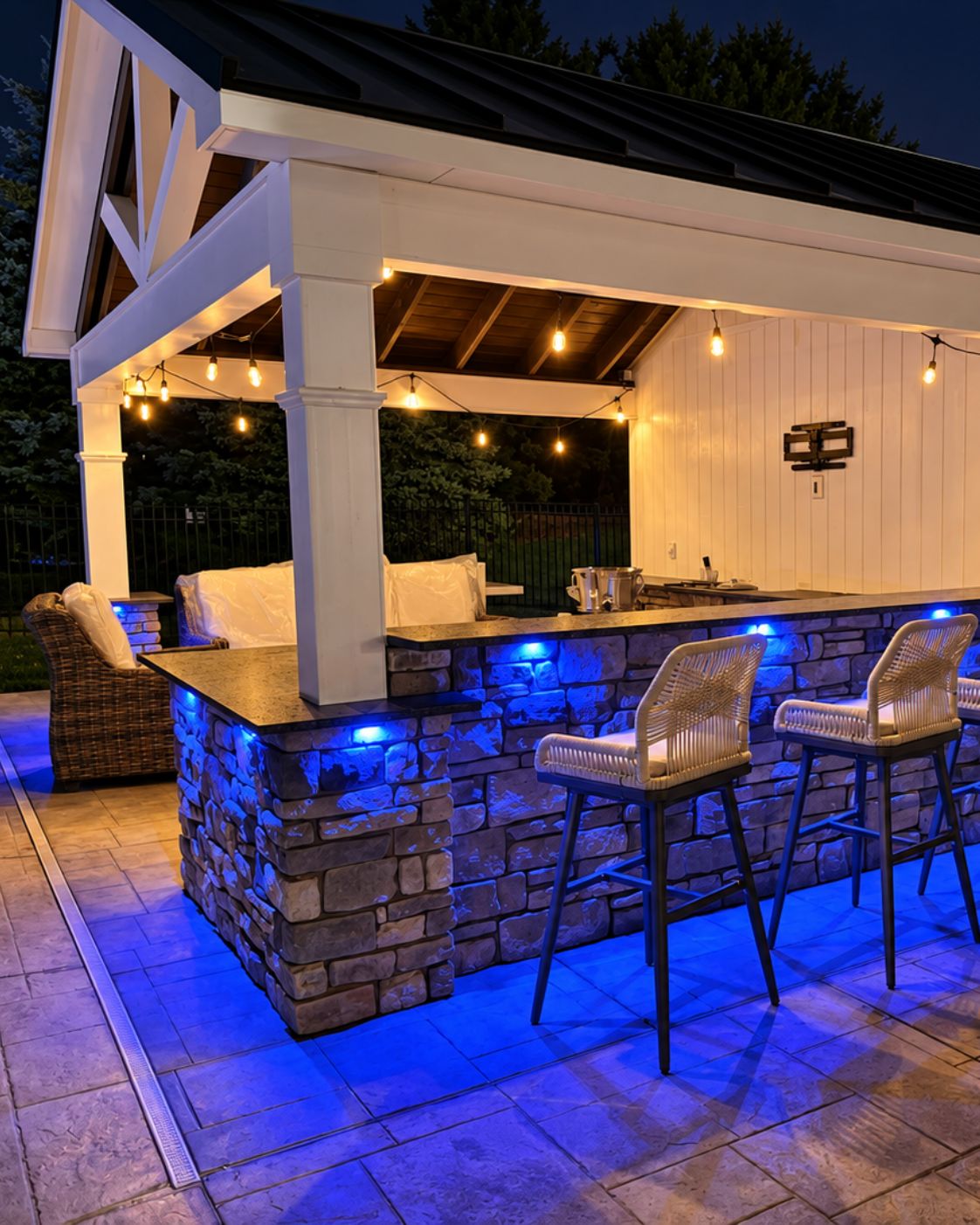 Finished outdoor pavilion with pool view, string lighting, and stone pillar accents by Canopy Building Services